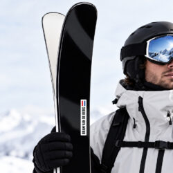 Naamlabels voor je ski's. Witte naamstickers op een zwarte ski. Vastgehouden door een man die de mooie bergen in de verte bekijkt.